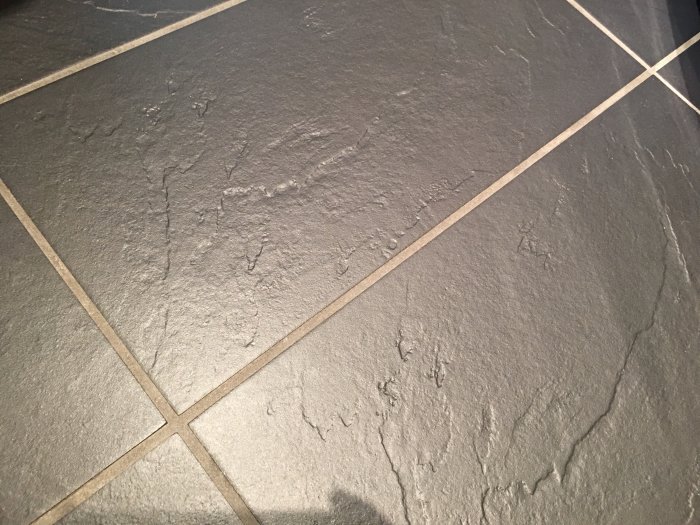 Mörkt klinkergolv i dusch med vita kalkfläckar och tydliga fogar.