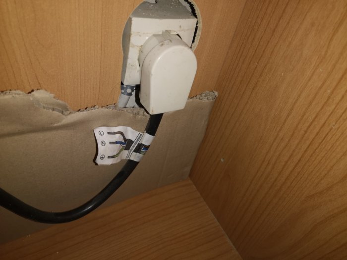 Elektrisk anslutning med öppen Perilex-kontakt, synliga ledningar och en etikett med kopplingsinstruktioner mot en trävägg.