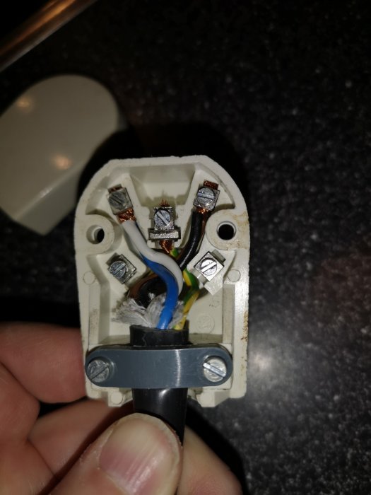 Närbild på öppen Perilex-kontakt med inkopplade ledningar och synliga kopplingsskruvar mot en svart bänkskiva.