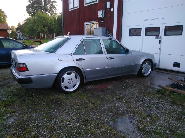 Silverfärgad Mercedes-Benz 500E parkerad utomhus bredvid en röd byggnad.