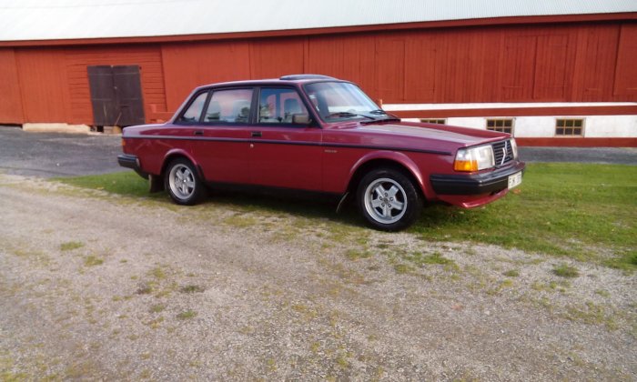 Röd Volvo klassisk sedanmodell parkerad framför röd lada, välbehållen efter 28 år.