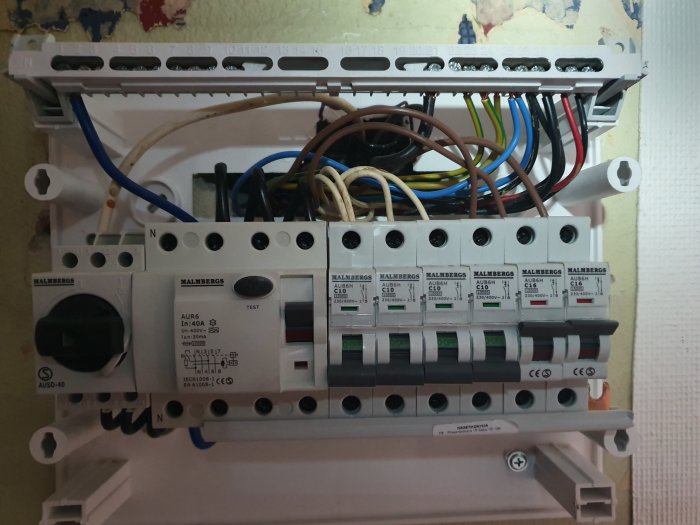 Öppen elcentral med flera säkringsautomater och trassliga kablar synliga i en oorganiserad installation.