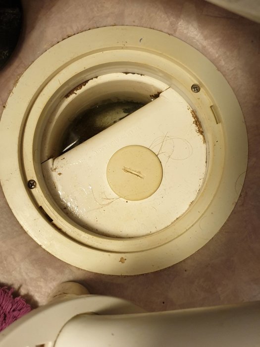 En golvbrunn i beige plast utan synligt vattenlås syns, omgiven av en golvplatta.