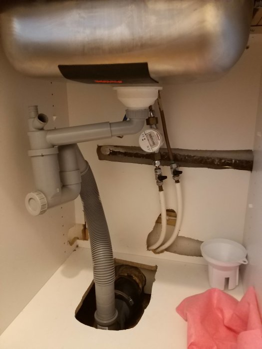 Undersida av diskho med rörkopplingar och vattenmätare, indikation på vattenläcka vid mutter.