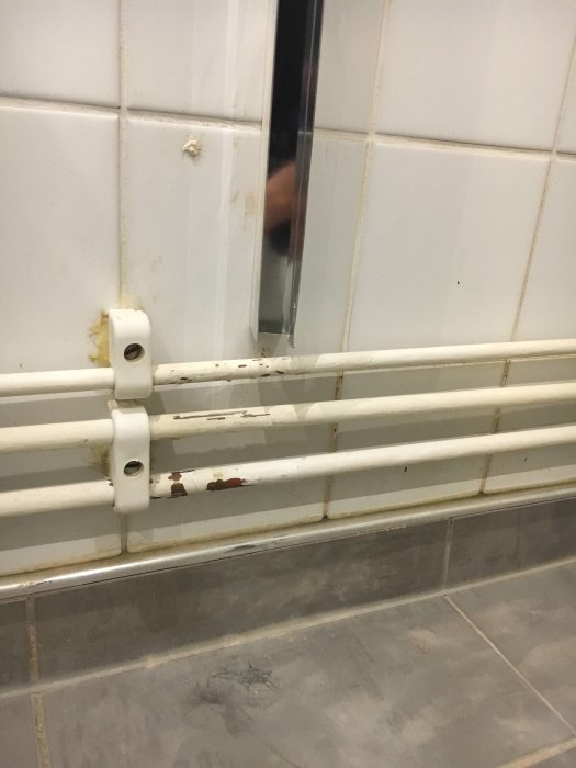 Skadad installation av en duschprofil vid kaklade väggen med synliga rör och ett borttaget kakelstycke.