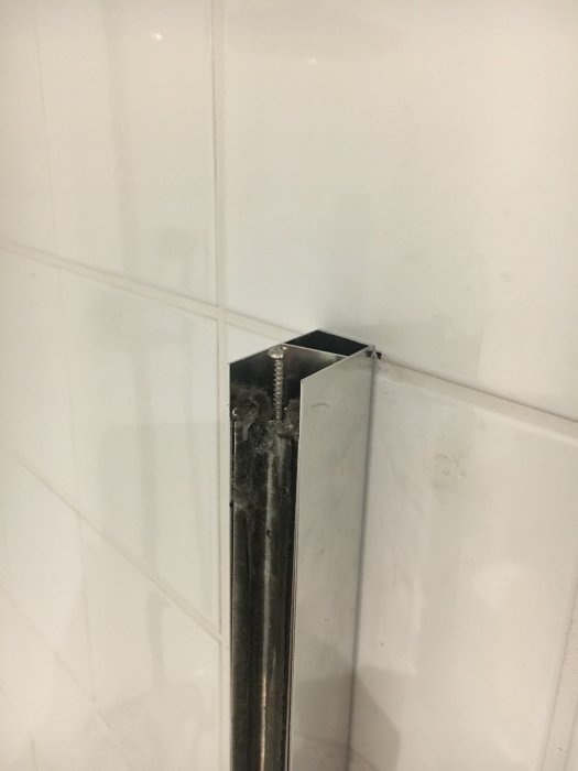 Felaktigt sågad duschhörnas profil mot kaklad vägg med synlig skada och avbruten rotation.