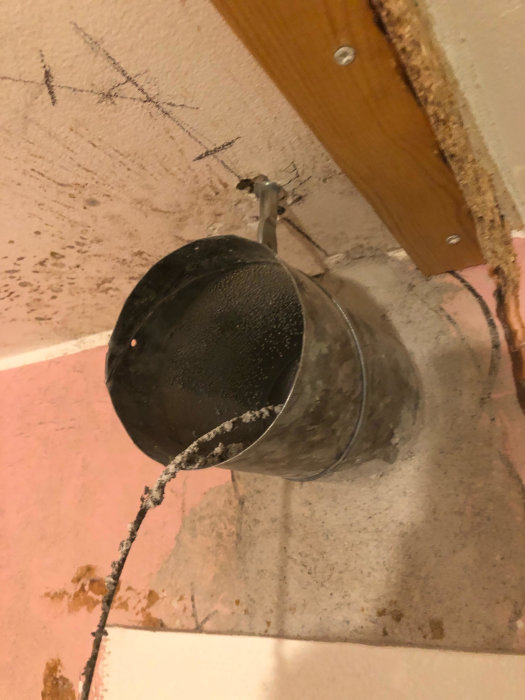 Ventilationsrör sticker ut ur en vägg, omgivet av spackel med spår av tidigare montering.