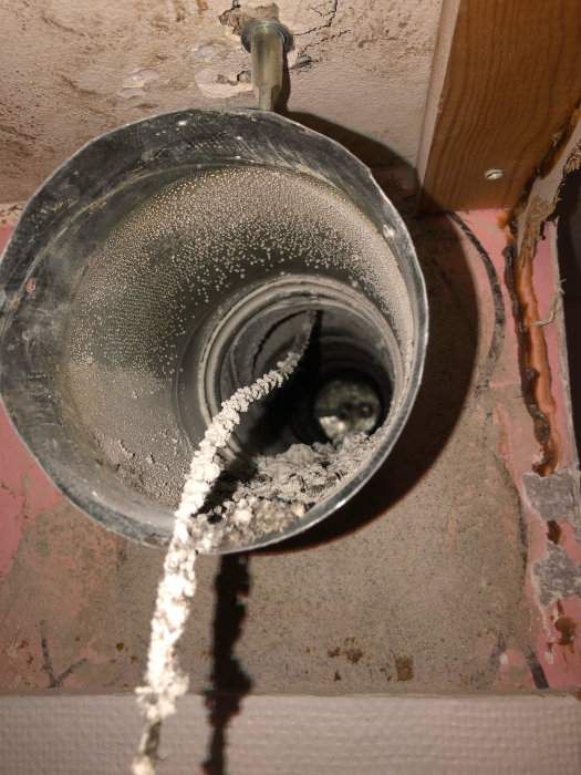 Utsnitt av ventilationsrör som sticker ut ur en vägg, omgiven av grov spackling.