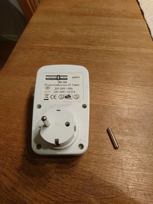 Elektrisk timer med ett kontaktstift lossnat, ligger bredvid på ett träbord.