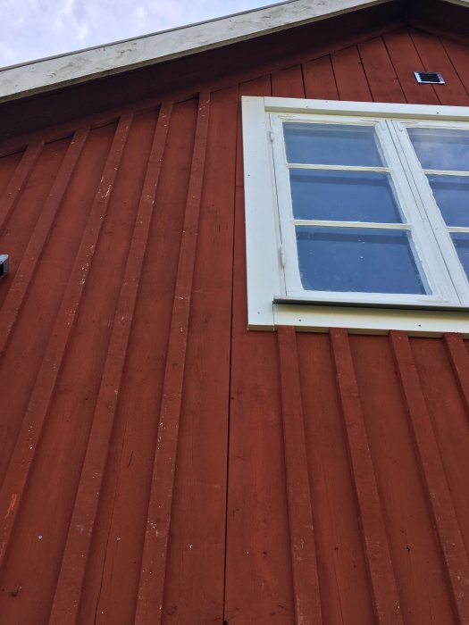Fasad med röda paneler och fönster där locklisten och panelen inte är riktigt raka.