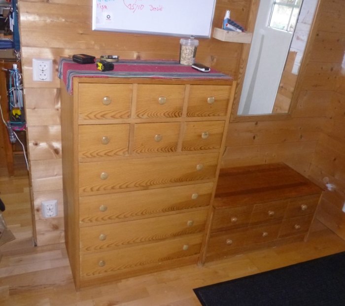 Två träbyråer med lådor i en hall, en används som sittplats med nycklar och ficklampor hängande intill.