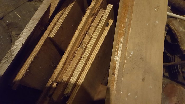 Staplar av gamla träbitar i olika storlekar och tillstånd på ett dammigt golv inne i en bod.