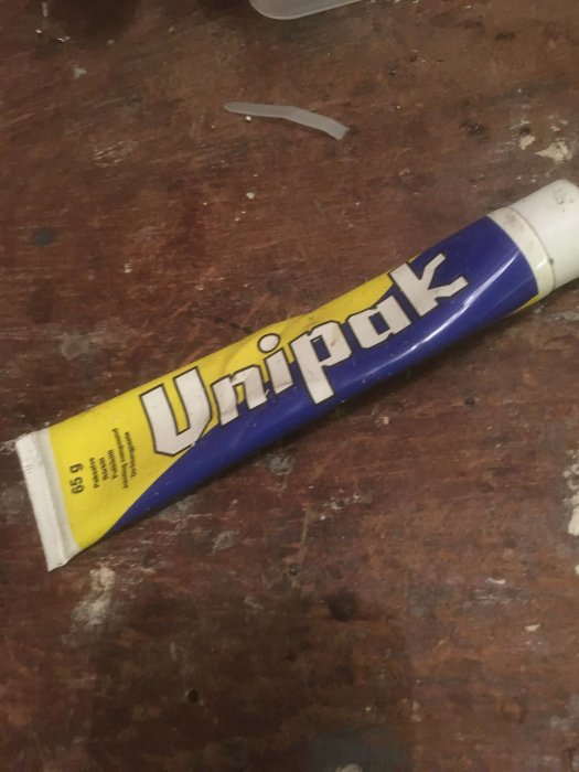 En tub oanvänd Unipak-tätningspasta på ett slitet träbord.