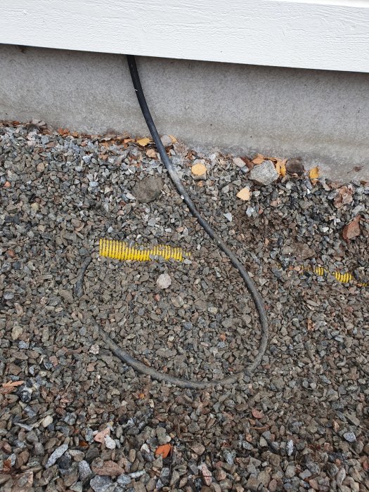 Elledning går längs marken bredvid en husgrund, delvis täckt av singel med synliga skyddsslangar som ligger löst ovanpå.
