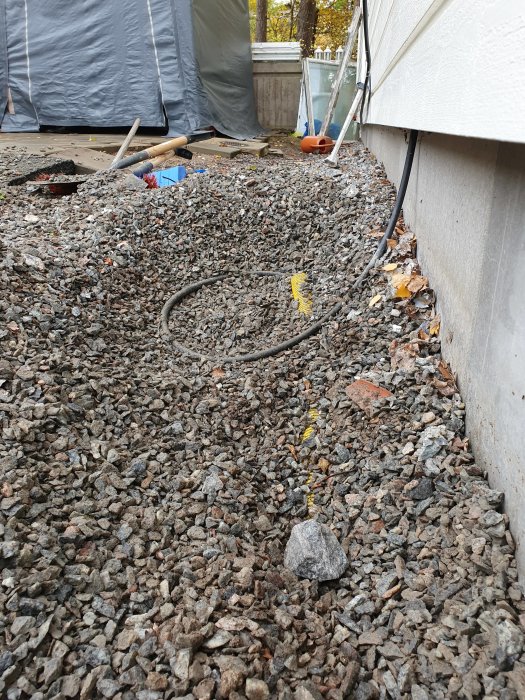 Elledning som löper längs med husgrund på en yta med singel; grävd del synlig med gul markering.