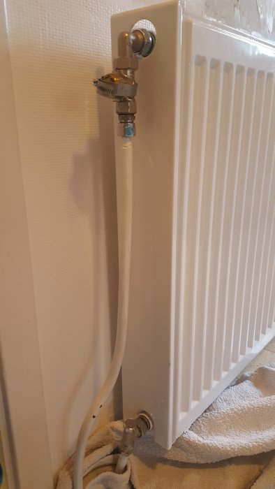 Väggmonterat vitt element utan synlig luftnippel, kopplingar syns upptill och nedtill.