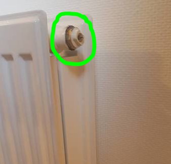 Luftnippel markerad med grön cirkel på en vit radiator, termostatens stift intryckt.