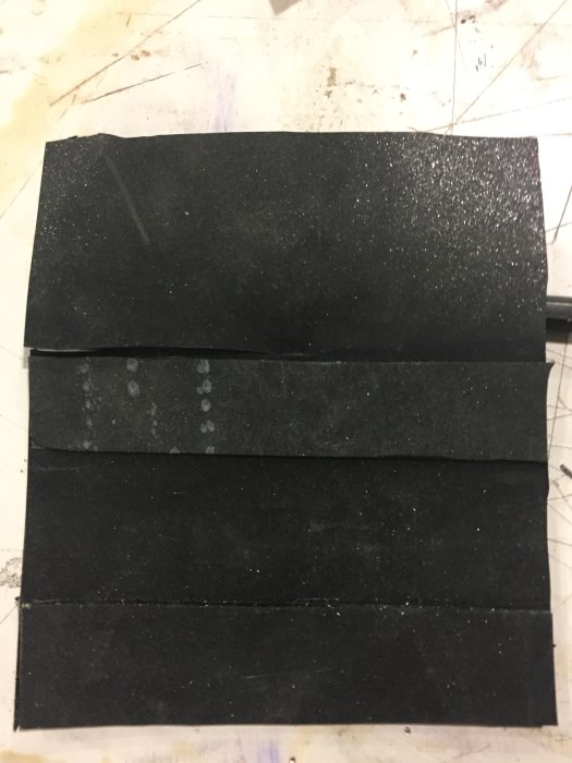 Svarta kardborreband ligger överlappande på ett smutsigt vitt underlag, använda för att tätning i verkstadsprojekt.