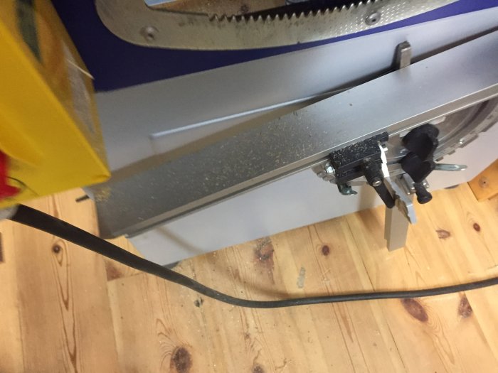 Delvis vy av en Metabo PKF 255 V8 formatsåg i en verkstad, visande sågklingan och spånsamling under arbetet.