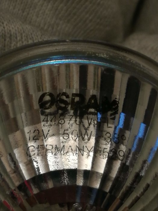 Närbild på en halogenlampa med speglig reflektor och specifikationer 12V 50W präglade på ytan.