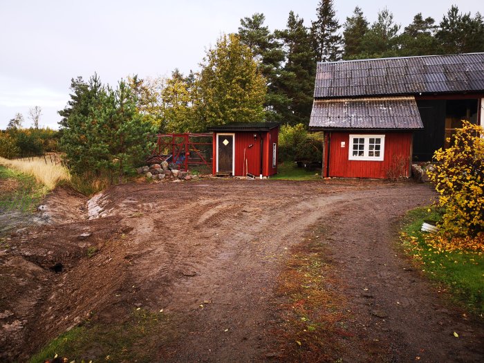 Nygrävda parkeringsplatser med synliga avloppsrör nära en röd stuga och uthus.