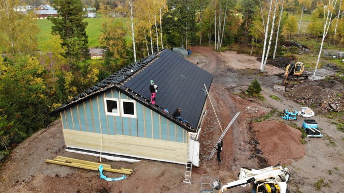 Installation av betongpannor på nybyggt hus, personer arbetar på taket med kranbil nära.