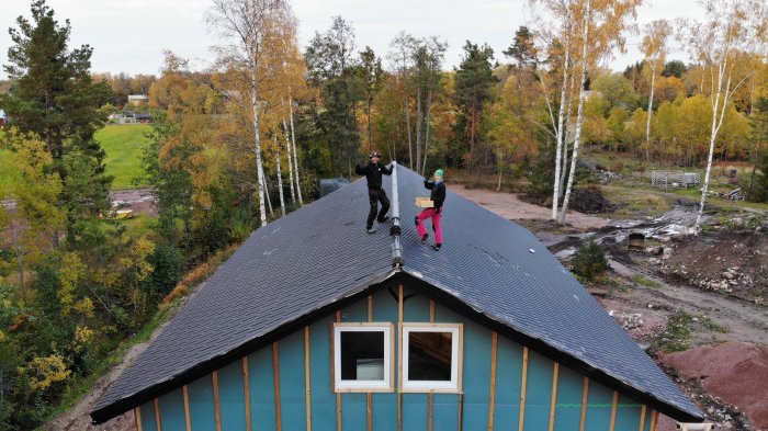 Nyinstallerade betongpannor på hustak med tre personer som jublar, omgivet av träd och landskap.