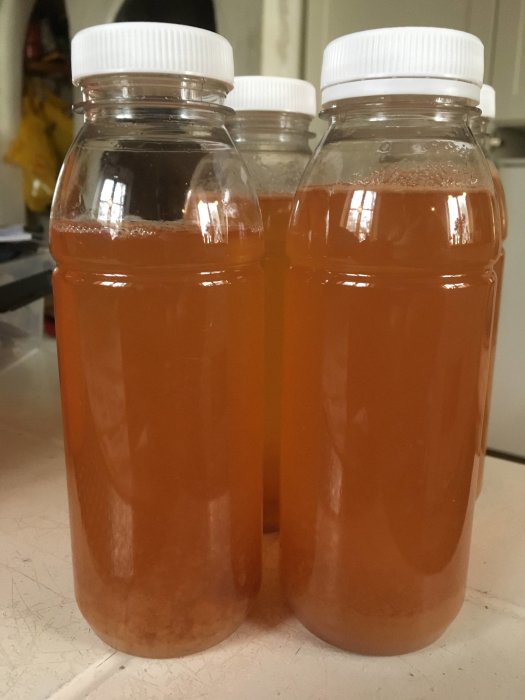 Tre flaskor med nypressad, hemgjord äppeljuice på en köksbänk.