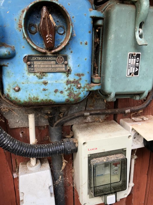 Slitna elektriska anordningar på en röd vägg inklusive en trefaskontakt, två säkringsskåp och en elmätare.