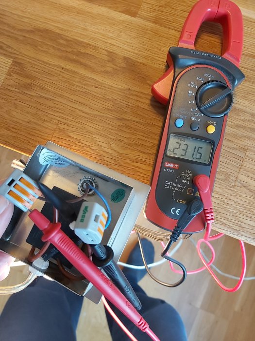 Mätning av spänning på eltrådar med multimeter som visar 231.6V, trådar ligger delvis utan skydd.