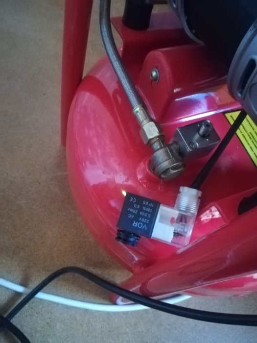 Röd JWS15 kompressor med sprucken manometer, kopplingar och sladdar synliga.
