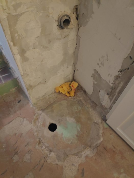 Nedfuktad källarhörna med upptäckt brunnsöppning i betonggolvet och inbyggd röranslutning i väggen.