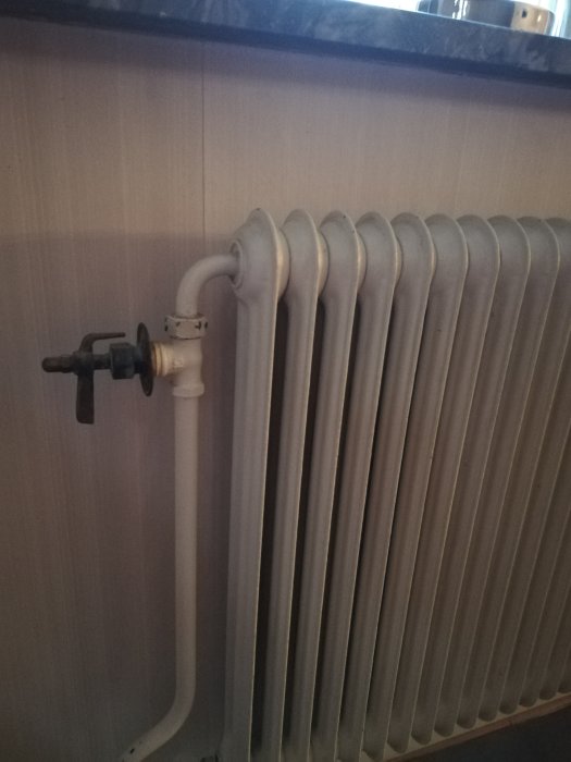 Gammaldags vit radiator med termostatventil mot en ljus väggbeklädnad, som del av diskussion om element i betonghus.