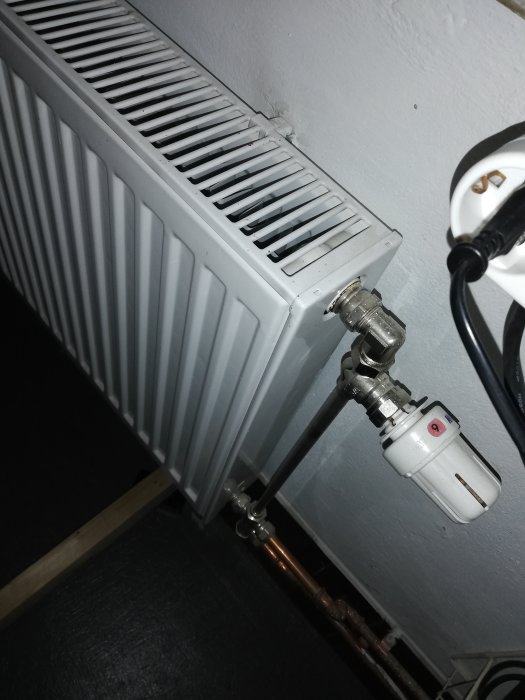 Radiator med termostat och anslutna kopparledningar mot betongvägg.