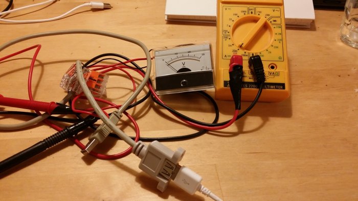 DIY elektronikuppställning med kablar, multimeter, och analog voltmätare för att testa laddspänning.