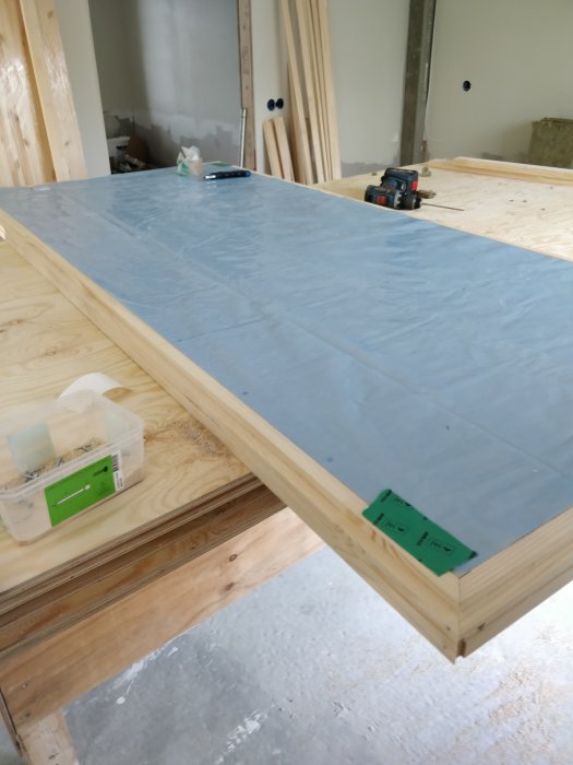 En påbörjad dörrkonstruktion med plywood på utsidan och ett färdigställd dörrblad som ligger på några trästöd.