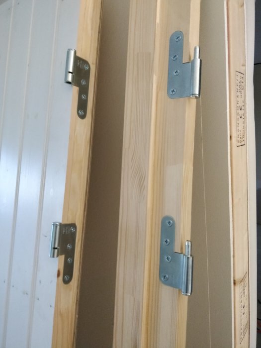 Närbild av en träddörr under tillverkning med infästa gångjärn och profillerade kanter.