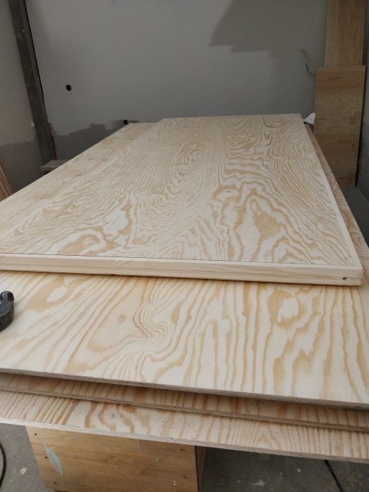 Utsida av handtillverkad dörr av plywood med spår för plåt, och verktyg synligt, i en snickarverkstad.