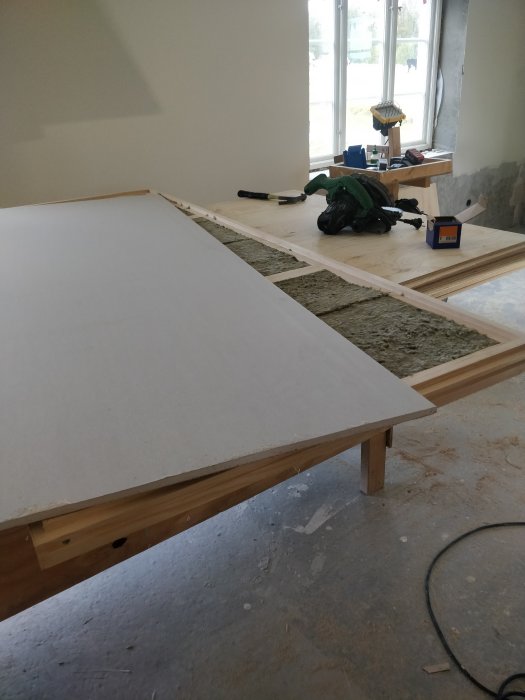Steg i tillverkning av en dörr: isolerat dörrblad med plywood och verktyg på arbetsbänk.