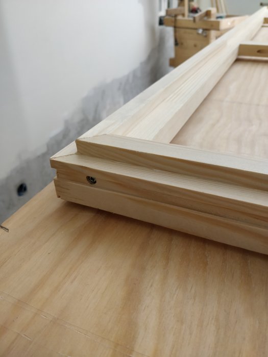 Detaljbild av hantverk i snickeri, träbitar till en dörrram ihopskruvade, stående på ett arbetsbord.