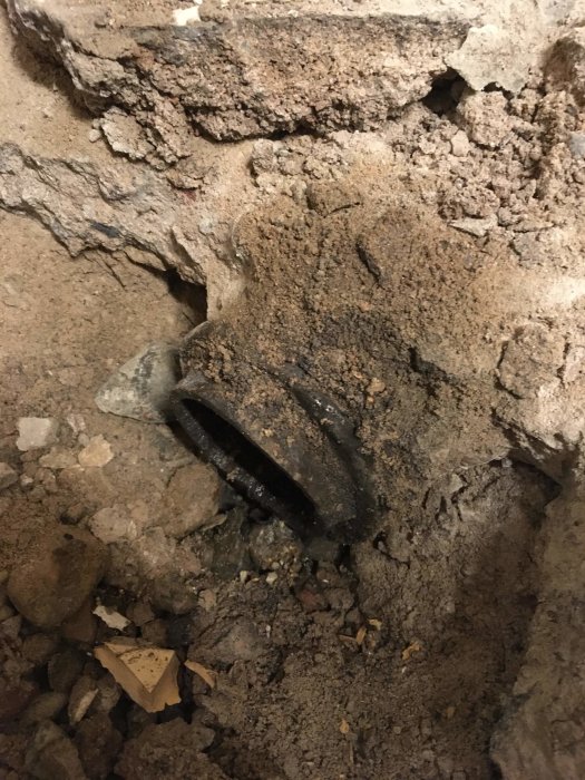 Golvyta med borttagen gjutjärnsbrunn och synlig järnmuff i en källare.