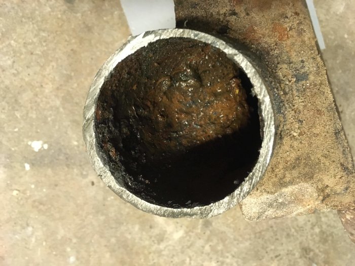 Närbild på kapat gjutjärnsrör i källare med tjockt, oanfrätt gods synligt.