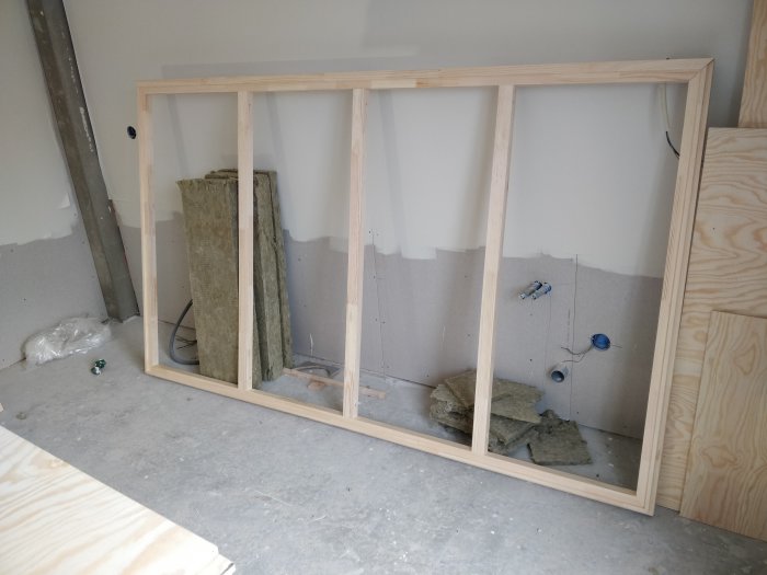 Dörrram av trä under konstruktion placerad mot en vägg med isoleringsmaterial och byggmaterial runtomkring.