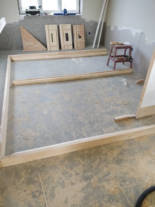 Träram på golvet och olika trädelar i bakgrunden av ett rum under renovering.