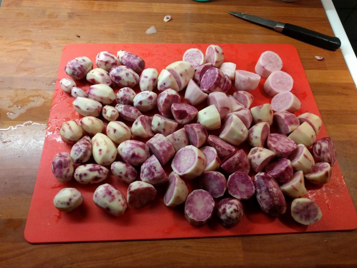 Skalade Highland Burgundy-potatisar på ett rött skärbräde och en kniv.