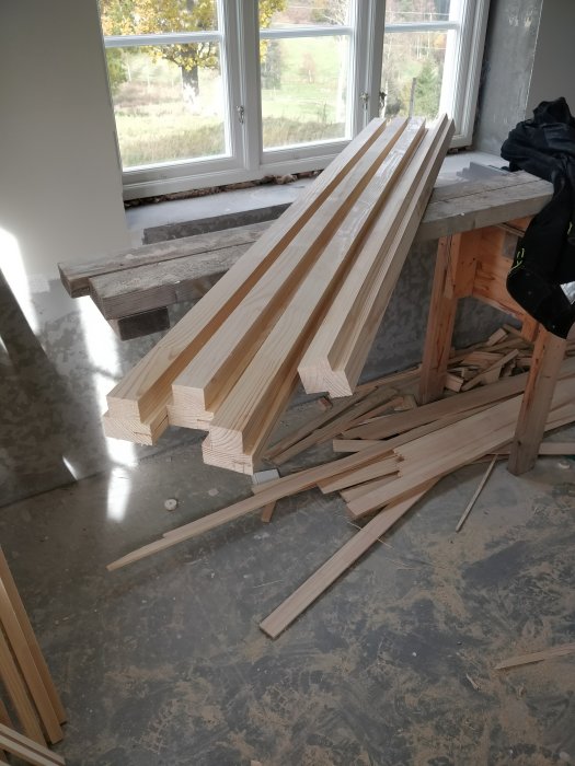 Träbitar till dörrram sågas till rätt profil på en arbetsbänk inne i ett rum under renovering.