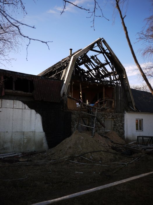 Delvis kollapsat gammalt hus med skadat tak och stegar, trolig följd av hemmagjord panna.