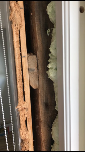 Insyn genom en luftspalt mellan stående träplank och isolering vid fönsterinstallation i ett äldre trähus.