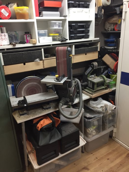 Överfylld sliphörna med tre olika slipmaskiner, dammsugarrör och verktygslådor på arbetsbord.