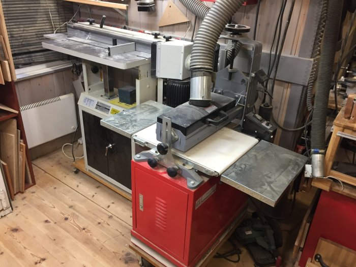 Tre olika slipmaskiner med dammsugarrör på ett trångt arbetsbord i en verkstad med trägolv.